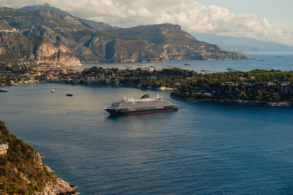 Explora Journeys EXPLORA II Ship cruise ship sailing in a calm bay surrounded by mountainous coastline and scattered smaller boats.