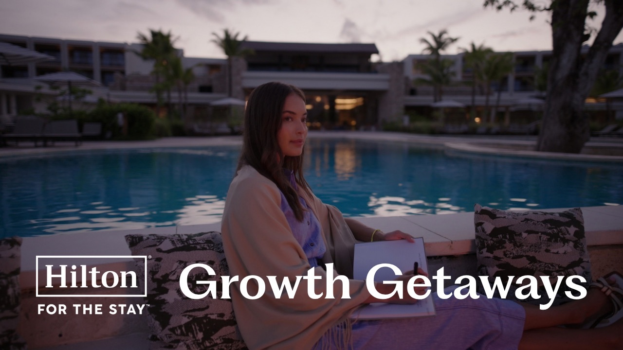 Woman sitting by a pool at dusk, writing in a notebook, with Hilton logo and "Growth Getaways" text overlay.
