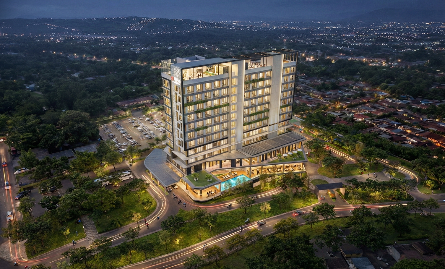 Modern Hilton Garden Inn Batam City Centre building with illuminated windows and a rooftop pool, surrounded by greenery and winding roads at dusk.