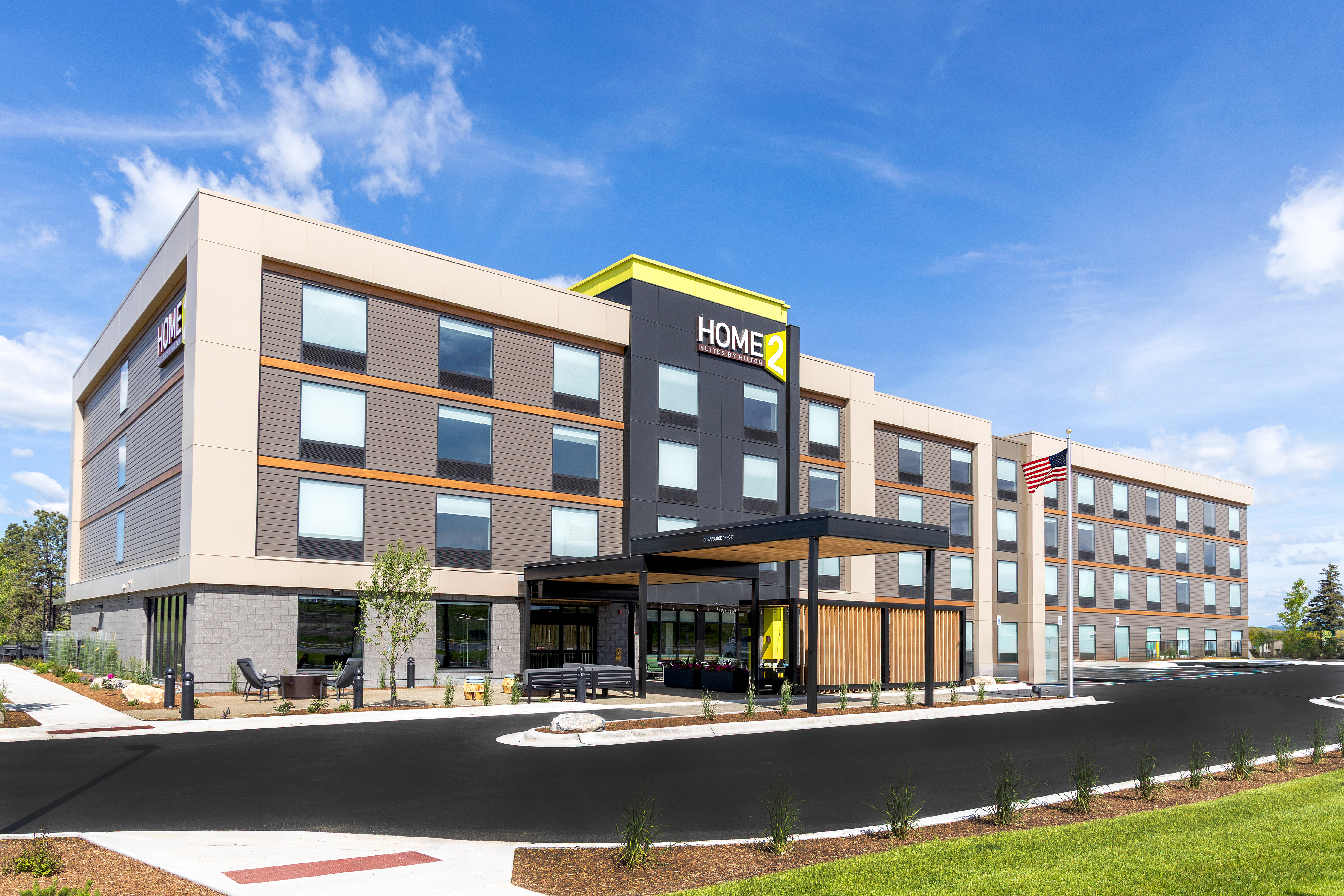 Modern four-story Home2 Suites by Hilton hotel with a covered entrance and an American flag on a flagpole.