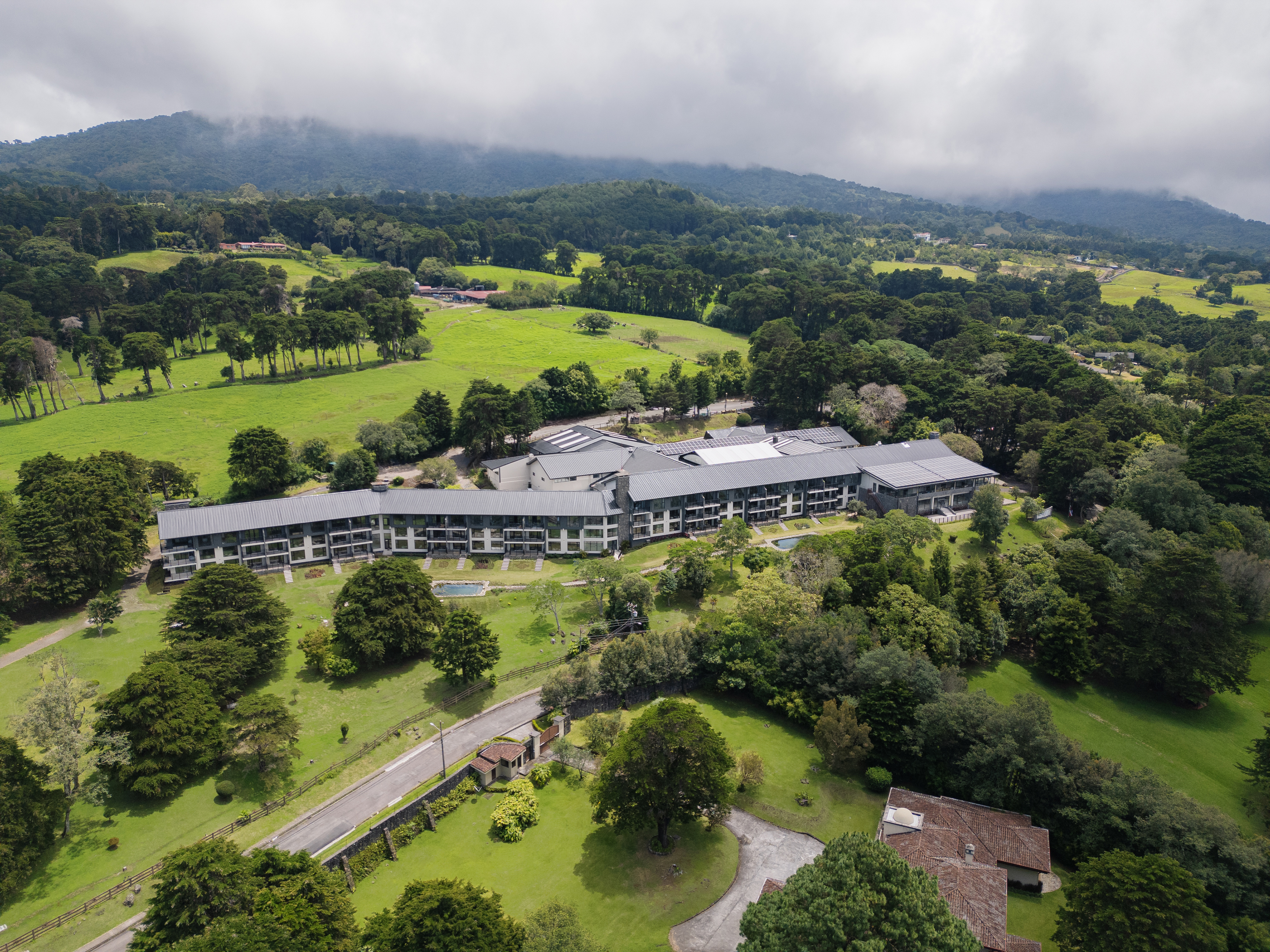 Large modern Montara Hotel, Tapestry Collection by Hilton hotel surrounded by lush green fields and dense forest with mist-covered hills in the background.