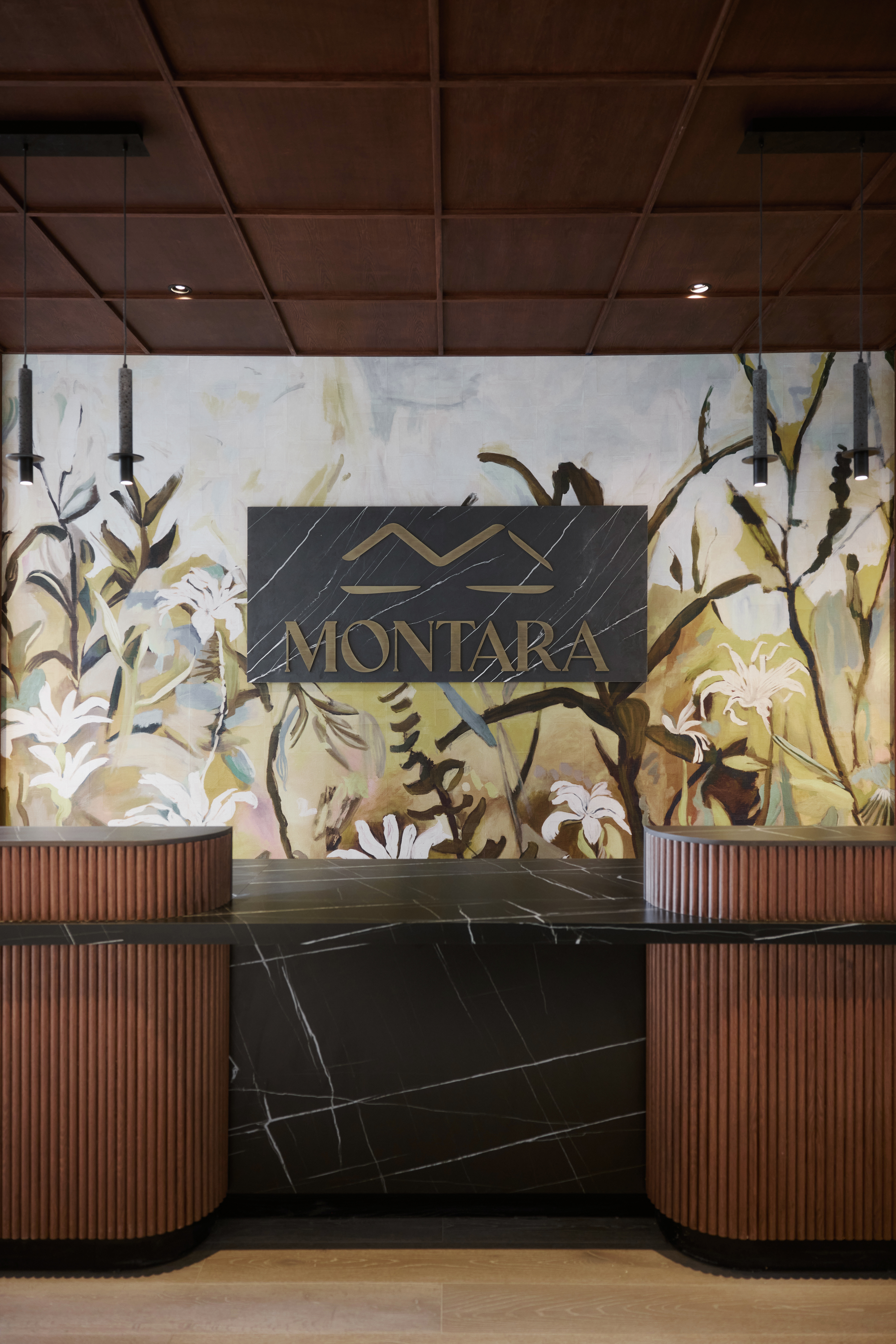 Reception desk at the Montara Hotel, Tapestry Collection by Hilton with a black marble front and wooden accents, set against a floral mural wall with a "MONTARA" sign above.