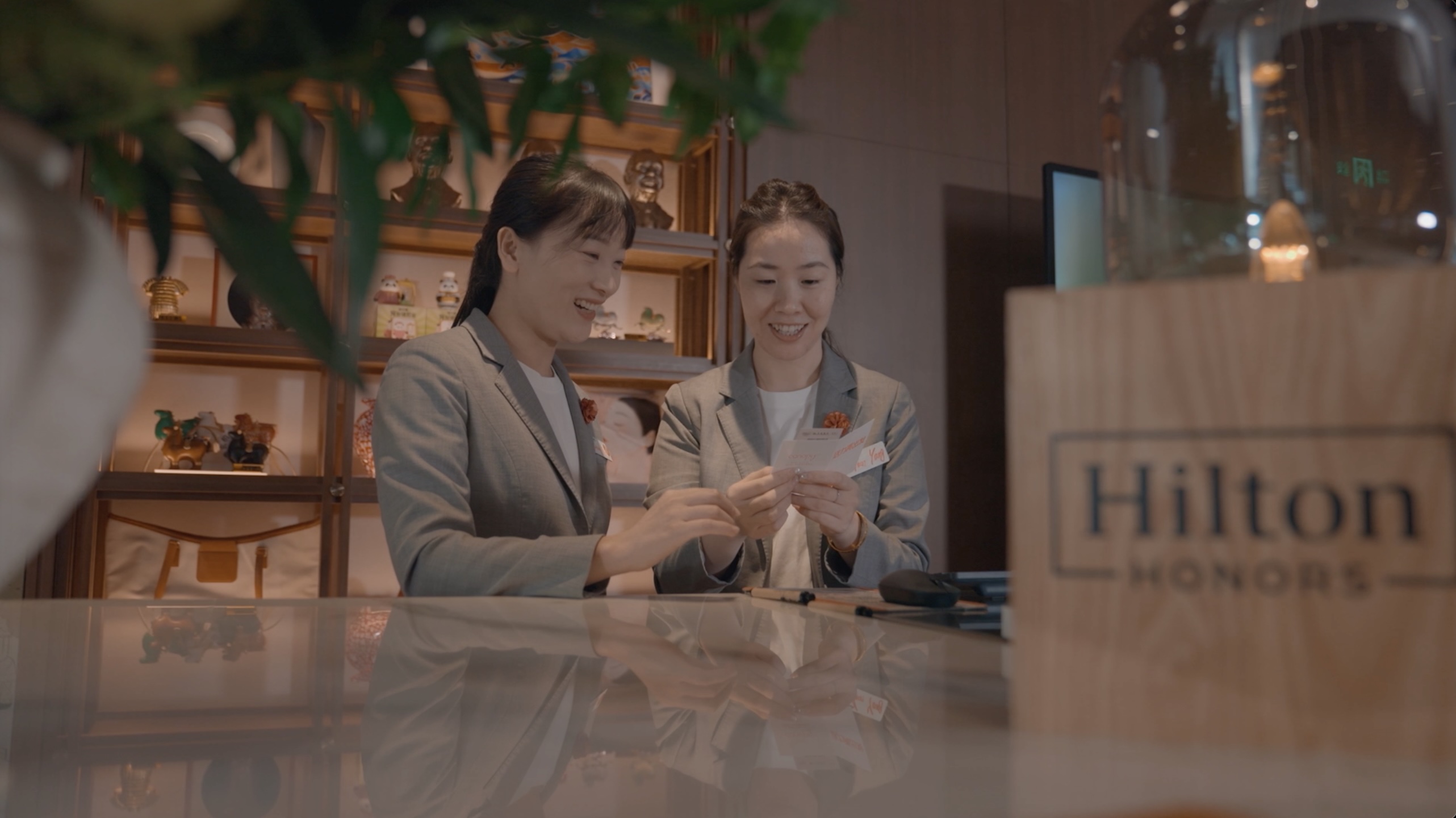 Two Canopy Xi’an Qujiang Team Members smiling and looking at cards behind a reflective counter with a Hilton Honors sign in the foreground.