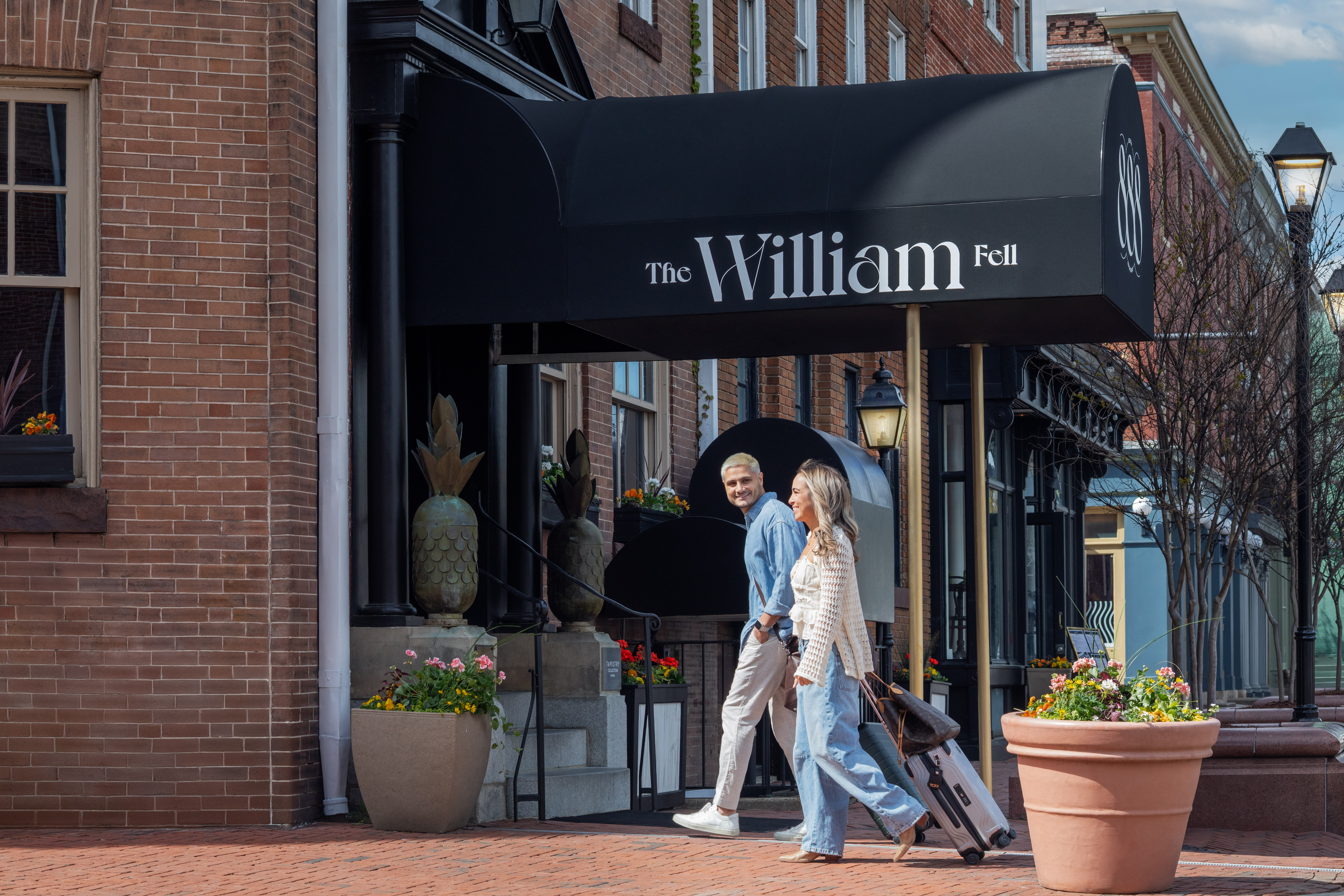 Two people walking with luggage outside The William Fell Baltimore, Tapestry Collection by Hilton